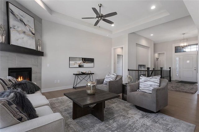 living room with dark wood-type flooring, a tiled fireplace, a tray ceiling, and a towering ceiling