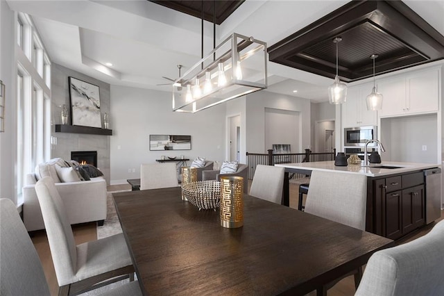 dining area featuring sink, a tiled fireplace, and a tray ceiling