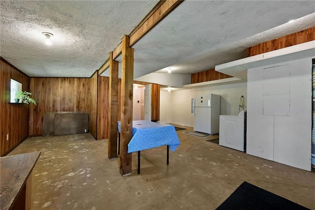 basement with wooden walls, white refrigerator, washer / dryer, and a textured ceiling