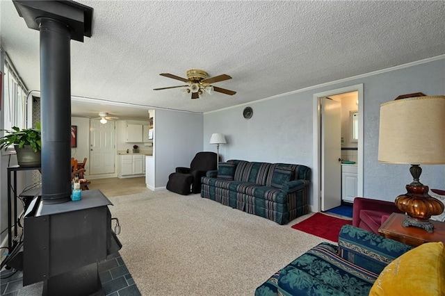 carpeted living room with ceiling fan, crown molding, a wood stove, and a textured ceiling