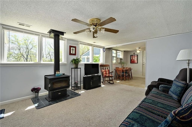 carpeted living room featuring ceiling fan, a wood stove, and a textured ceiling