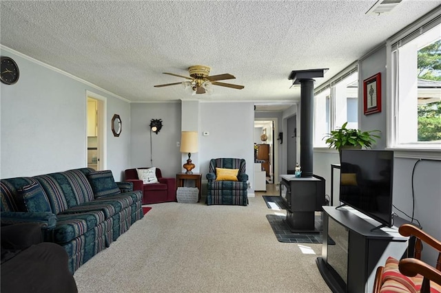 carpeted living room with a textured ceiling, a wood stove, ceiling fan, and crown molding