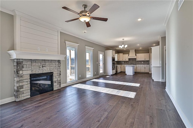 unfurnished living room featuring a fireplace, ornamental molding, dark wood-type flooring, and ceiling fan with notable chandelier