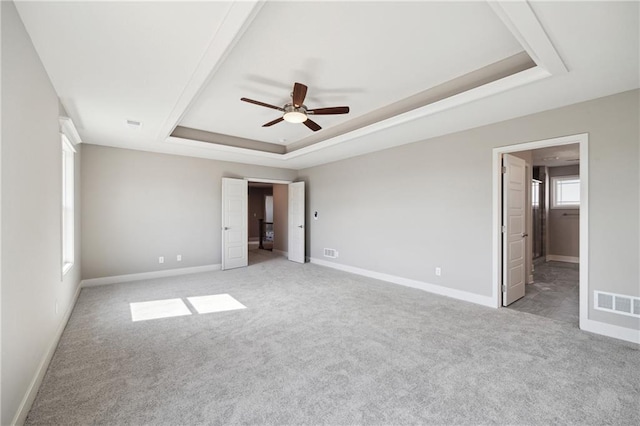 unfurnished bedroom featuring ceiling fan, light carpet, and a tray ceiling