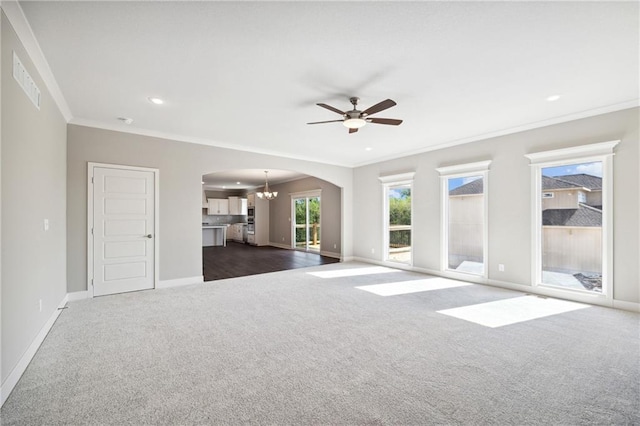 unfurnished living room with ceiling fan with notable chandelier, dark colored carpet, and crown molding