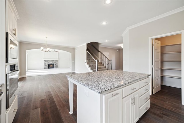 kitchen featuring a stone fireplace, white cabinets, crown molding, a center island, and dark hardwood / wood-style flooring