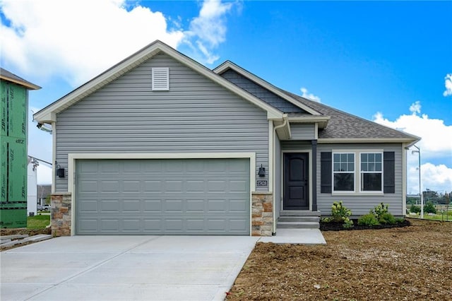 view of front of property with driveway, stone siding, an attached garage, and a shingled roof