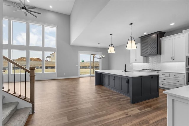 kitchen featuring pendant lighting, an island with sink, white cabinets, dark hardwood / wood-style flooring, and decorative backsplash