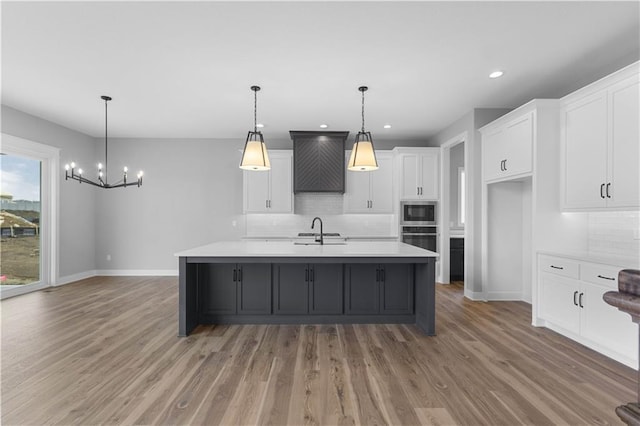 kitchen featuring a kitchen island with sink, decorative light fixtures, oven, and built in microwave