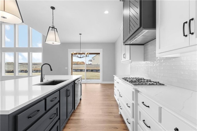 kitchen featuring sink, appliances with stainless steel finishes, white cabinets, decorative light fixtures, and wall chimney exhaust hood