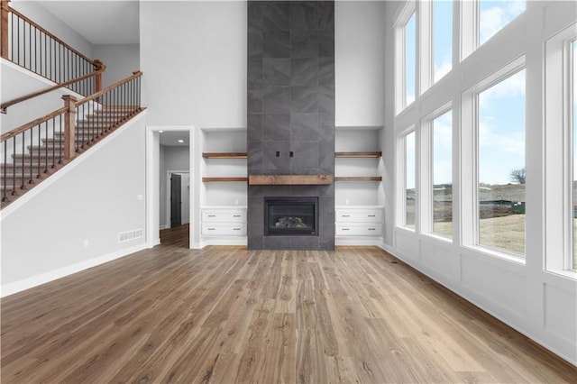 unfurnished living room with a fireplace, a high ceiling, and light wood-type flooring