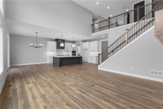 unfurnished living room featuring hardwood / wood-style floors, a towering ceiling, sink, and a chandelier