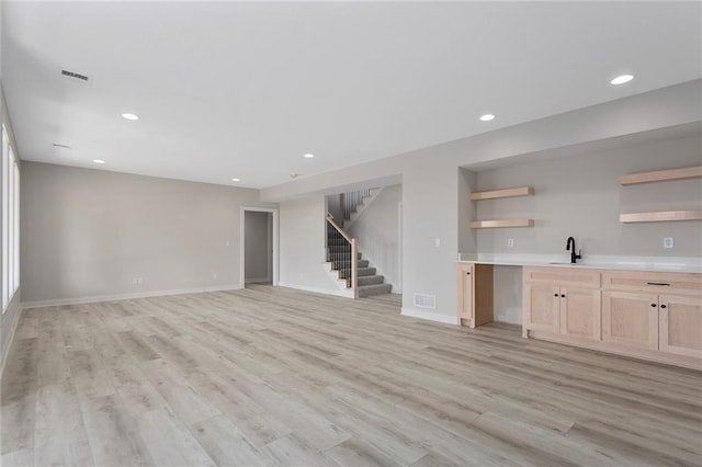 unfurnished living room featuring light wood-type flooring, stairway, a sink, and recessed lighting