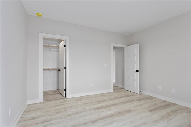 unfurnished bedroom featuring baseboards, a closet, a walk in closet, and light wood-style floors