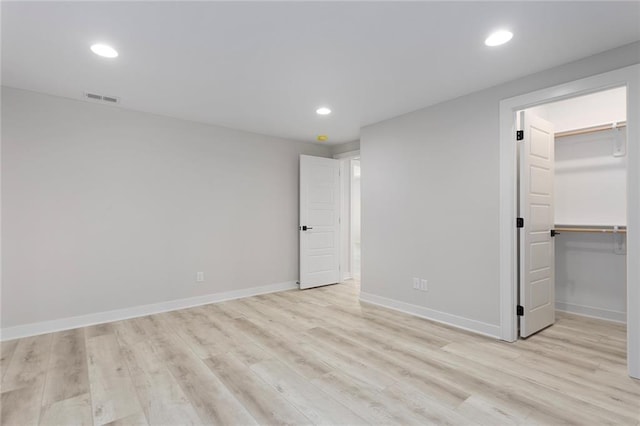 unfurnished bedroom with recessed lighting, a walk in closet, light wood-style flooring, and baseboards