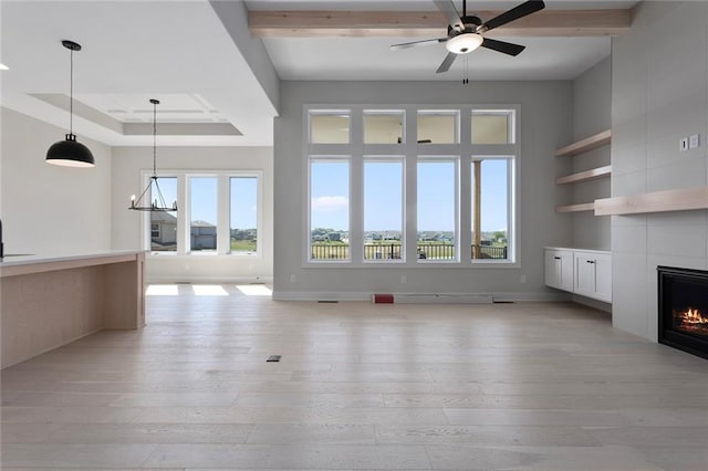 unfurnished living room featuring a fireplace, light wood finished floors, a raised ceiling, baseboards, and ceiling fan with notable chandelier