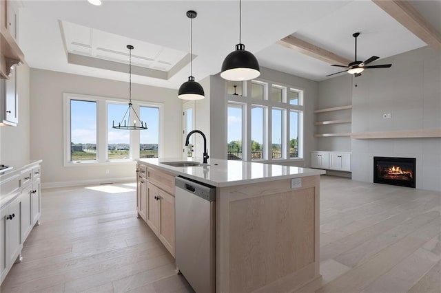 kitchen with a tiled fireplace, dishwasher, light wood-style flooring, a tray ceiling, and a sink