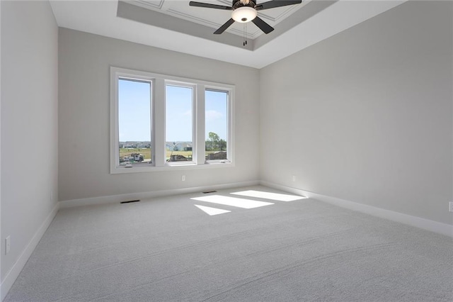 unfurnished room with a tray ceiling, visible vents, carpet flooring, ceiling fan, and baseboards