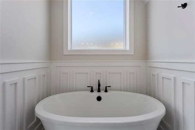 bathroom with a wainscoted wall, a freestanding bath, and a decorative wall