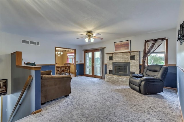 living room featuring carpet floors, ceiling fan with notable chandelier, and a brick fireplace