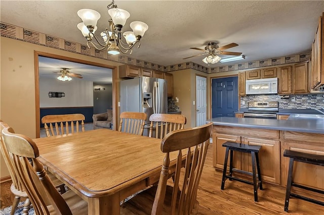 dining space featuring a textured ceiling, ceiling fan with notable chandelier, and light hardwood / wood-style flooring