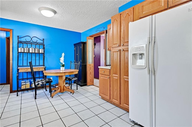 kitchen featuring a textured ceiling, light tile flooring, and white refrigerator with ice dispenser