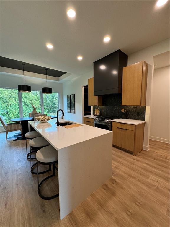 kitchen with sink, premium range hood, decorative light fixtures, a center island with sink, and light wood-type flooring