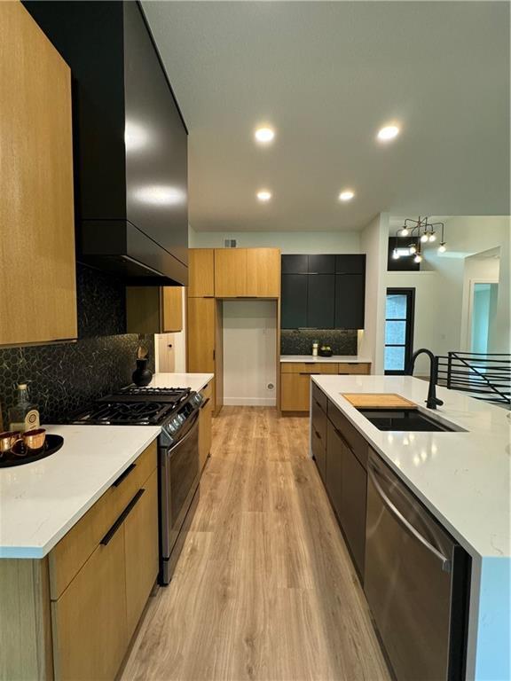 kitchen featuring decorative backsplash, appliances with stainless steel finishes, light wood-type flooring, sink, and an island with sink