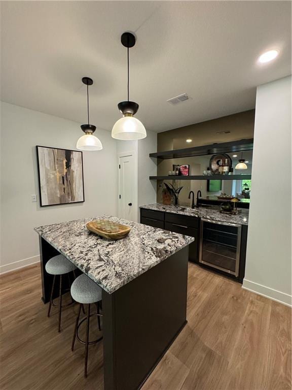 bar with sink, wine cooler, light stone counters, pendant lighting, and light hardwood / wood-style floors