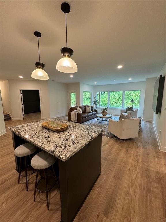 kitchen with pendant lighting, a kitchen island, light stone countertops, and light wood-type flooring