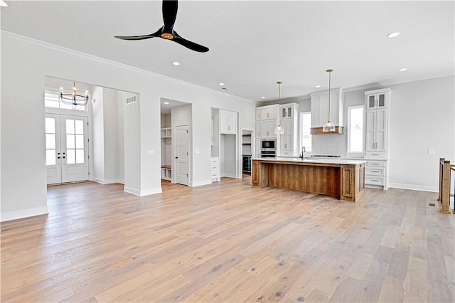 kitchen featuring white cabinets, ceiling fan with notable chandelier, decorative light fixtures, ornamental molding, and a large island