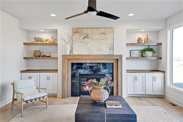 living area with built in features, light hardwood / wood-style floors, and ceiling fan