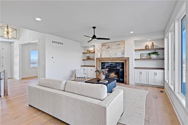 living room featuring ceiling fan with notable chandelier, built in features, and light hardwood / wood-style floors