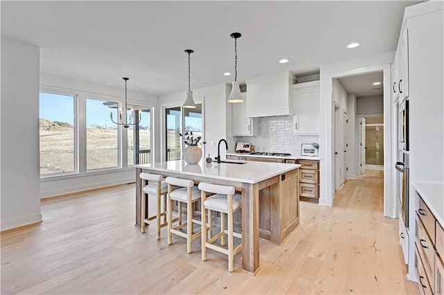 kitchen with sink, an island with sink, custom range hood, white cabinets, and backsplash