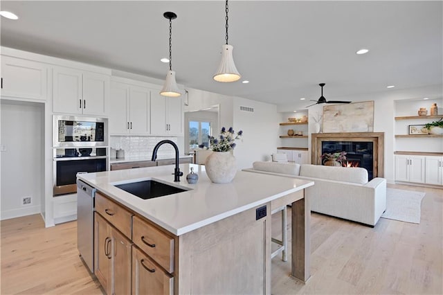 kitchen featuring appliances with stainless steel finishes, pendant lighting, white cabinetry, sink, and a kitchen island with sink