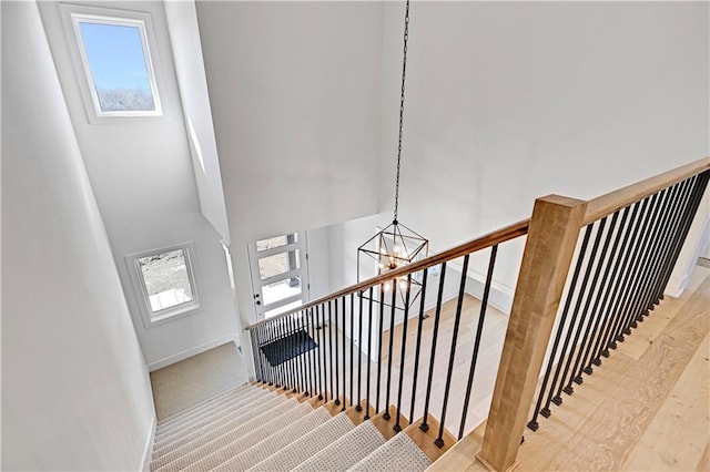 stairs with plenty of natural light, a chandelier, wood-type flooring, and a high ceiling