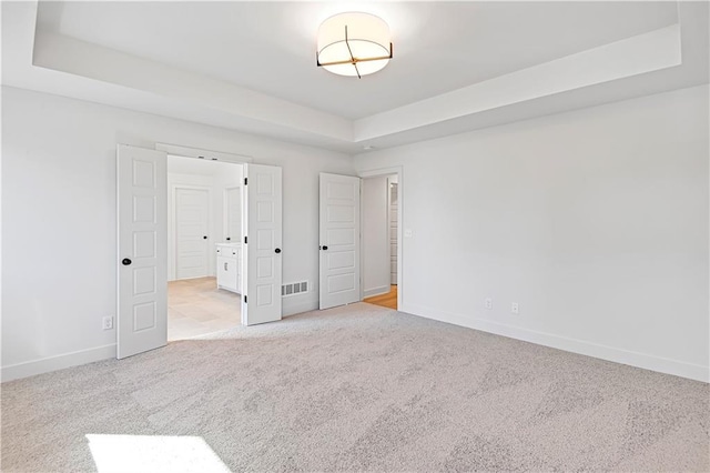 unfurnished bedroom featuring light colored carpet and a raised ceiling