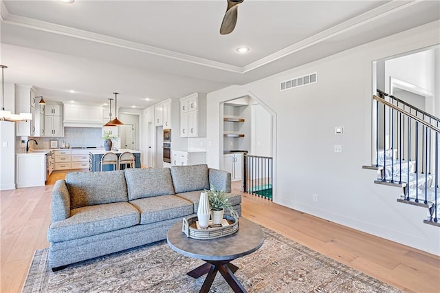 living room featuring ceiling fan, ornamental molding, a tray ceiling, and light hardwood / wood-style flooring