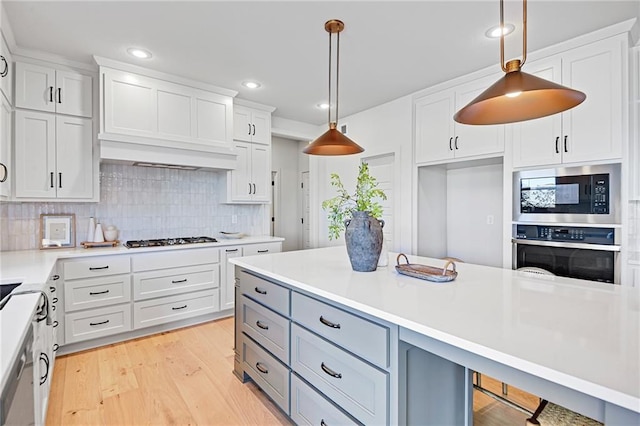 kitchen featuring pendant lighting, appliances with stainless steel finishes, light wood-type flooring, and white cabinets