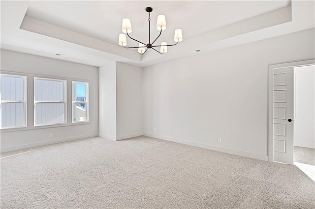 carpeted spare room with a notable chandelier and a tray ceiling