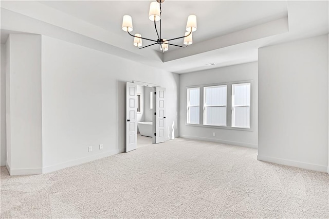 carpeted empty room with a notable chandelier and a tray ceiling