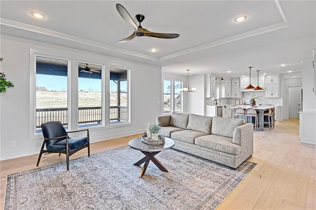 living room with crown molding, ceiling fan, a raised ceiling, and light hardwood / wood-style flooring