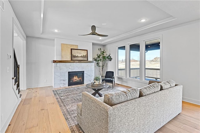 living room featuring ceiling fan, a fireplace, a raised ceiling, and light hardwood / wood-style flooring