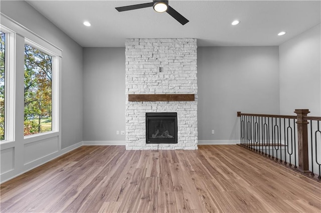 unfurnished living room with light wood-type flooring, a stone fireplace, and ceiling fan