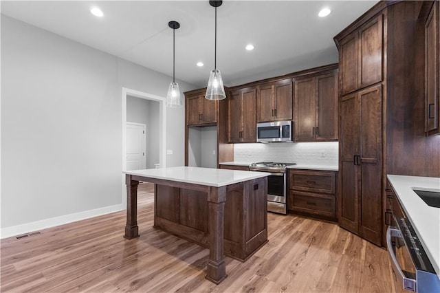 kitchen featuring a kitchen bar, appliances with stainless steel finishes, tasteful backsplash, pendant lighting, and light hardwood / wood-style floors