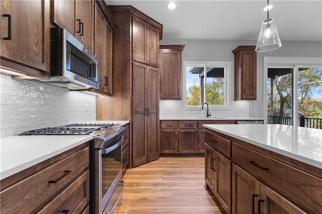 kitchen with decorative backsplash, stainless steel appliances, sink, light hardwood / wood-style floors, and hanging light fixtures