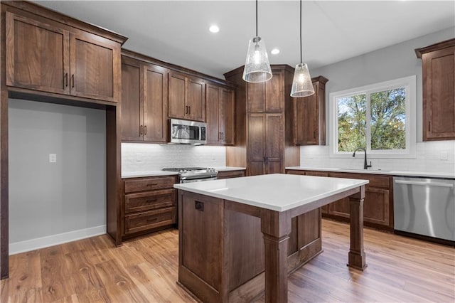 kitchen with sink, a center island, pendant lighting, appliances with stainless steel finishes, and light wood-type flooring