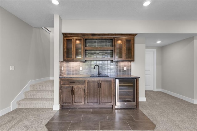 bar with sink, beverage cooler, decorative backsplash, dark brown cabinets, and dark carpet