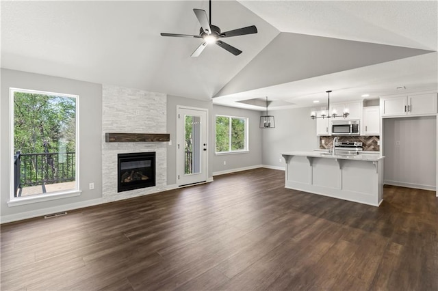 unfurnished living room featuring high vaulted ceiling, ceiling fan with notable chandelier, sink, a fireplace, and dark hardwood / wood-style flooring