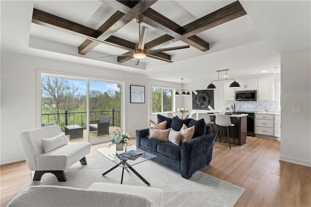 living area featuring beam ceiling, light wood finished floors, ceiling fan, and coffered ceiling